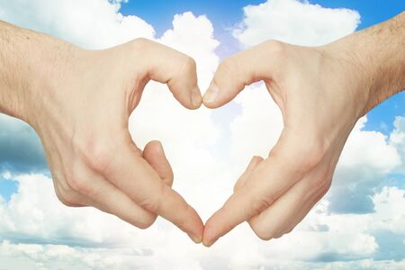 Hands make heart shape against blue sky backgroundの写真素材