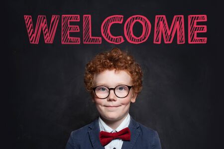 Smiling child with ginger hair portrait. Cute little boy in blue suit against blackboard with...