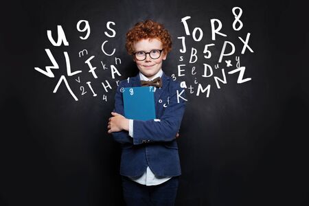 School boy in blue student uniform with book on blackboard background