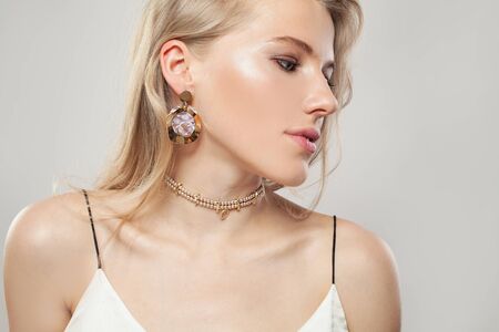Gold jewelry model. Beautiful blonde woman with golden earrings and necklace on white background. Perfect female profileの写真素材