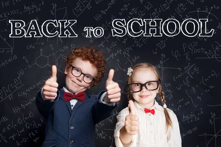 Successful clever children in school uniform showing thumb up on blackboard background, back to school and science power conceptの写真素材