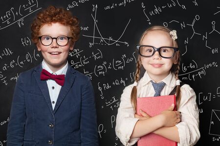 Smiling kids in school uniform on blackboard background with science formulas, back to school conceptの写真素材