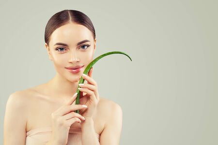 Beautiful young woman with clear skin holding green aloe vera leaf. Skincare and facial treatment conceptの写真素材