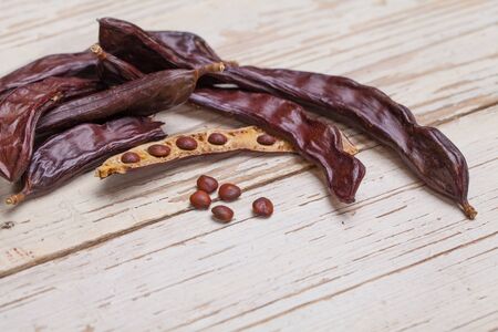 Carob. Organic carob pods with seeds and leaves on white wooden table. Healthy eating, food background.の写真素材
