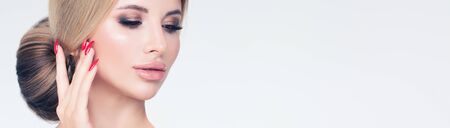 Fashion portrait of beautiful blonde woman face closeup on white banner background. Trendy hairstyle and red manicured nails on handsの写真素材