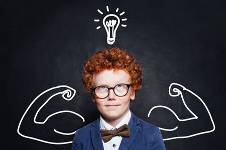 Cute boy with lightbulb on blackboard background. Brainstorming and idea concept