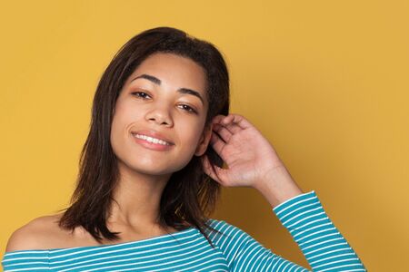 Pretty young woman wearing blue clothes smiling and posing on yellow background