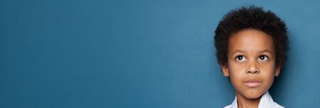 Cute small black child boy looking up on blue banner background with copy spaceの写真素材