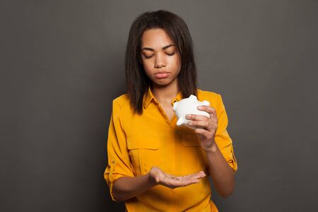 Sad black woman holding empty piggy bank and getting upset