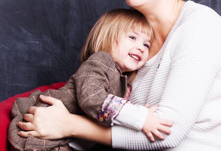 People and family concept. Happy smiling girl with mother hugging on armchair