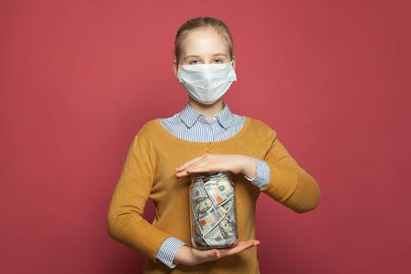 Girl in medical mask holding money cash us dollars on blue backgroundの写真素材