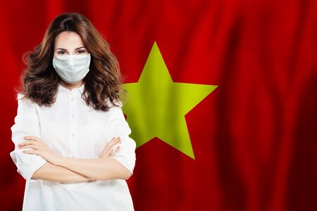 Doctor in protective face mask against national flag Vietnam. Flu epidemic and virus protection conceptの写真素材