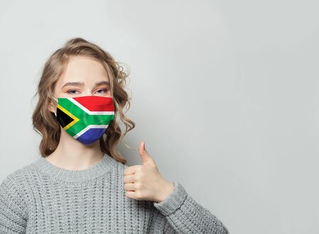 Happy woman in face mask holding thumb up with national flag background. Flu epidemic and virus protection conceptの写真素材
