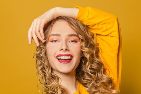 Happy woman with long curly hair smiling on bright yellow background