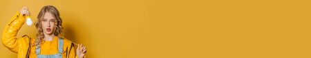 Young woman with lightbulb on yellow banner background with copy spaceの写真素材