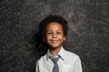 Happy smart black child student on blackboard background with science and maths formulasの写真素材