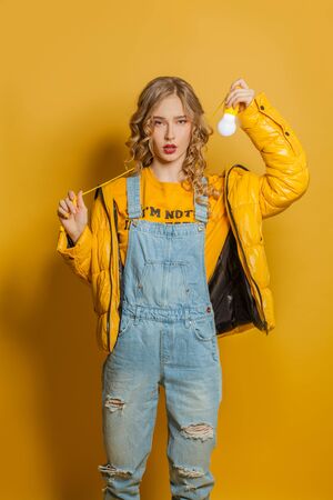 Young woman in yellow sweatshirt holding lightbulb on yellow backgroundの写真素材