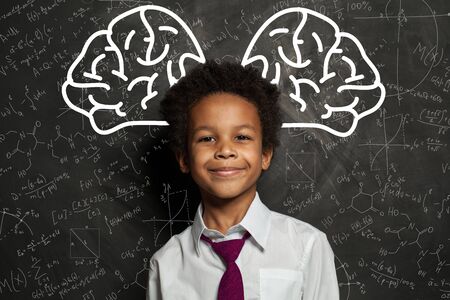 Clever child. Little school boy student on chalkboard background with big brain and science formulas