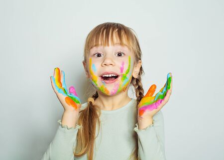 Happy surprised little girl with colorful painted hands drawing. Pretty child art school student on white backgroundの写真素材
