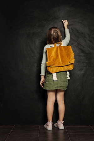 Girl drawing with chalk on empty school blackboard background