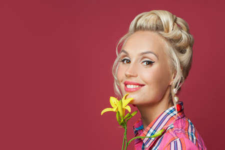 Smiling pinup woman fashion model with yellow flower on red background. Happy retro woman closeup...