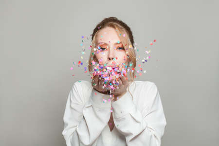 Attractive woman blowing colorful confetti on gray banner backgroundの写真素材