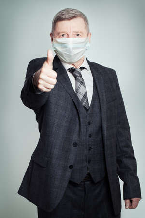 Happy older man in medical face mask showing thumb up on white backgroundの写真素材