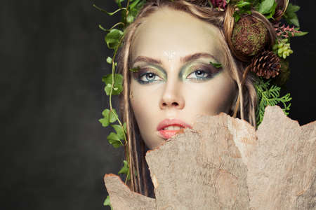 Beautiful woman with creative makeup, green leaves and tree bark. Halloween characterの写真素材