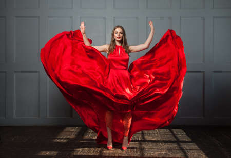 Happy woman in blowing red silky dress posing indoorsの写真素材