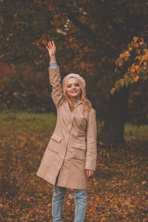Happy autumn woman waiving saying hello and smiling outdoor, friendly welcome gestureの写真素材