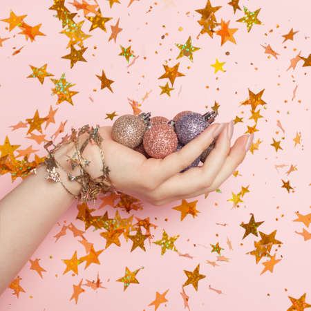Christmas decoration in female hand on pink card background with golden confetti starsの写真素材