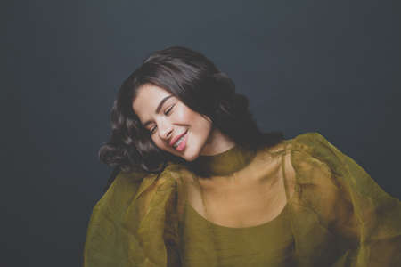 Laughing woman with dark brown curly hair in green dress on black backgroundの写真素材