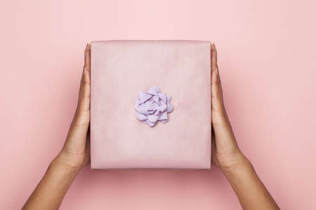 Beautiful minimal background composition with hand holding gift on pastel pink color