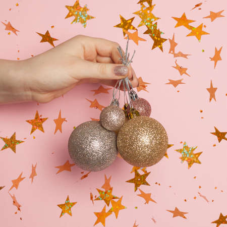 Christmas or New Year confetti stars and Xmas balls in woman hand on pink card backgroundの写真素材