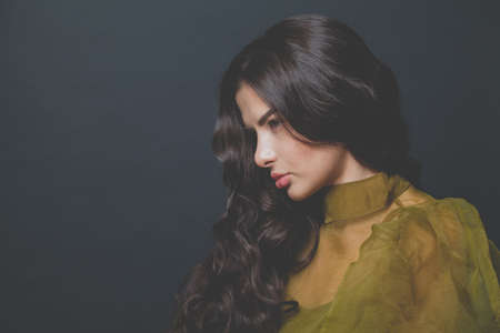 Attractive brunette woman fashion model with long healthy curly hair on black backgroundの写真素材