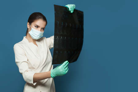 Doctor in protective medical mask holding computed tomography scan on blue background