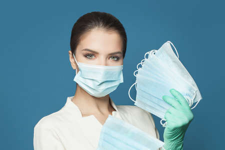 Doctor holding many protective medical masks on blue background. Medicine and safety concept