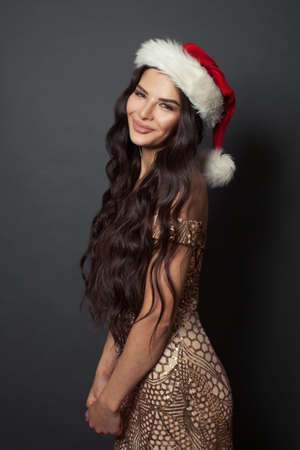 Pretty woman Santa in gold evening gown on black background. Christmas holiday and New Year party portraitの写真素材