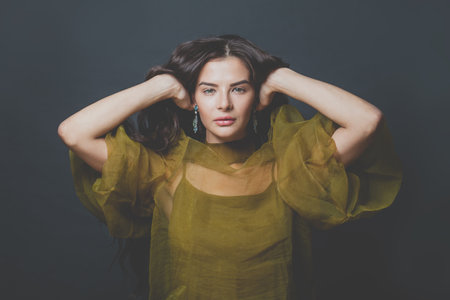 Stylish fashionable brunette model woman with long curly hair in green tulle evening gown on black backgroundの写真素材