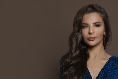 Fashion model woman brunette with long curly hair on brown background, beauty portraitの写真素材