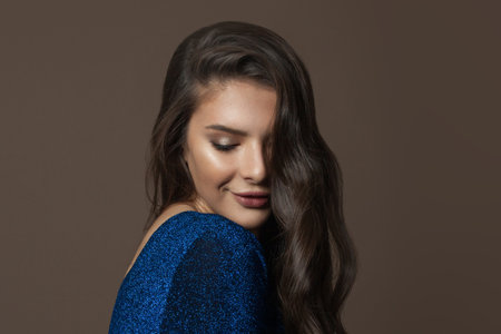 Beautiful face with healthy clear skin, long curly hair and natural makeup on brown backgroundの写真素材