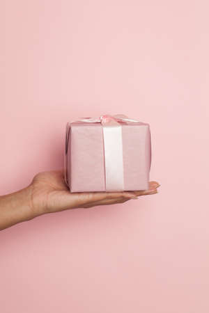 Hand holding gift box on pink backgroundの写真素材