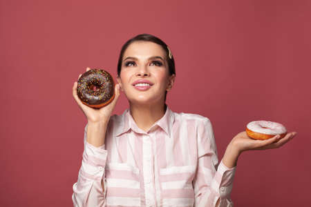 Beautiful woman holding donuts an having fun on pink background. People with sweetsの写真素材
