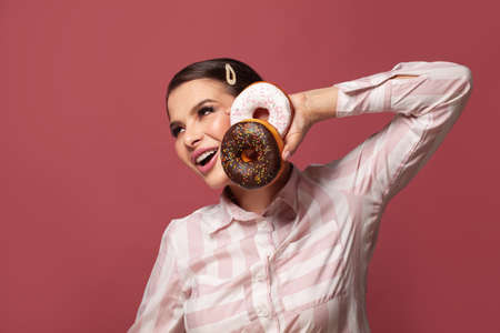 Attractive woman holding donuts and having fun on red background, diet and weight loss conceptの写真素材