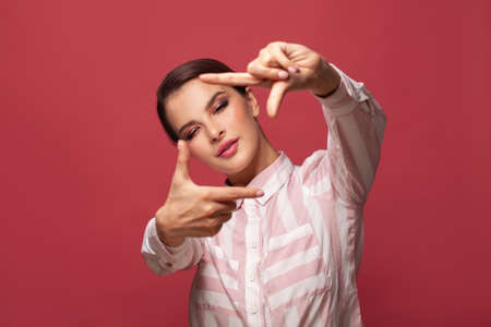 Young woman over red wall smiling and making photo gesture
