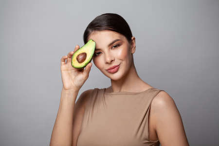 Close up photo beautiful lady smiling holding slice avocado on gray background. Cheerful woman, healthy eating, dieting and detox conceptの写真素材