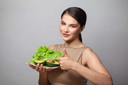Happy woman showing thumb up and holding green avocado with salad. Detoxification, vegetarian, healthy eating and diet conceptの写真素材