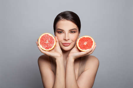Young woman with fruits on gray background. Pretty model showing grapefruits, portraitの写真素材