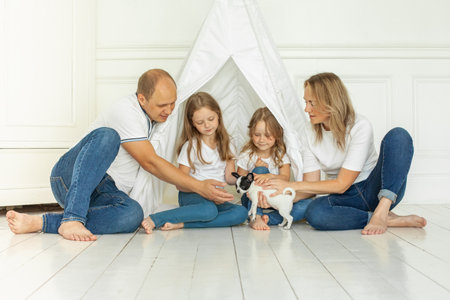 Happy young mother and father with two little daughters sitting on floor, looking at little puppy dog petの写真素材