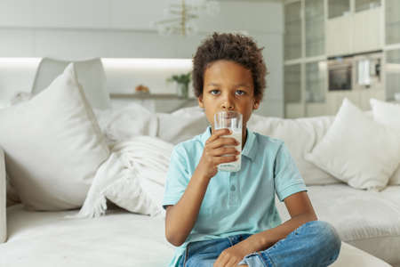 Cute little boy drinking milk from glass indoorの写真素材